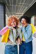 © Jose Calsina - Joyful women sharing a delightful shopping experience, showcasing their colorful bags and infectious smiles, embodying friendship and excitement in a lively moment of happiness together.