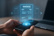 © Aimo Studio - Person using smartphone to view digital invoices with laptop in the background on a wooden table