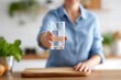 © ryker - Close up of elegant hand holding up glass of clear water, showcasing refreshing drink in bright kitchen setting. atmosphere feels inviting and healthy