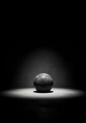 Poster - Sphere in Dark Studio Lighting - A single dark grey sphere sits centrally in a spotlight against a dark background. It symbolizes simplicity, mystery, focus, elegance, and potential