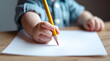 © Oksana - A child's hand holds a pencil on a blank sheet of paper.