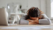 © JoeyMarut - Woman resting head on folded arms at desk with laptop, showing tiredness and exhaustion in bright office environment