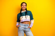 © deagreez - Stylish young woman with braided hair in casual attire posing confidently against a vibrant yellow background