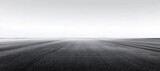 Vast empty asphalt road stretches to the horizon under a clear, bright sky, creating a minimalist and expansive landscape image.