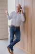 © Tj - Senior businessman leaning against a wooden wall while talking on the phone and gesturing with his hand, looking confident and engaged in conversation