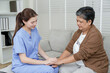 © Ekkasit A Siam - Asian female physiotherapist sitting on sofa gently holding hands of senior asian woman while engaging in caring conversation during supportive therapy session in peaceful rehabilitation room