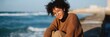 © Andrii Zastrozhnov - Smiling african female young adult sitting by the ocean on a breezy day