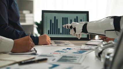 Poster - A robotic hand gestures toward business charts during a collaborative team meeting, highlighting the blend of technology and human effort in data analysis.Noogenesis