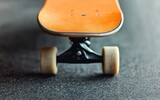 Close-up of an orange skateboard deck with white wheels on a textured asphalt surface.