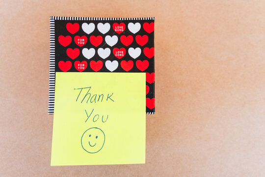 Thank you note that says thank you handwritten with blue pen with a background of a gift box with red and white hearts
