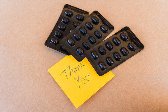 Thank you note that says thank you handwritten with blue pen with a background of an oximeter and pills