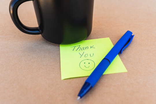 Thank you note that says thank you handwritten with blue pen with a coffee cup background