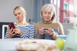 © JackF - Mature woman with her adult daughter, sitting at a table in a room, looking at photos on a mobile phone