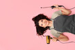 © Pixel-Shot - Happy young female hairdresser with hair dryer and curling iron lying on pink background