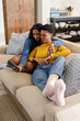 © Wavebreak Media - Diverse female couple leaning together on beige sofa in living room puckering lips at smartphone