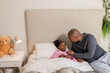 © Wavebreak Media - African American father and daughter sitting on bed feeding medicine by spoon beside nightstand