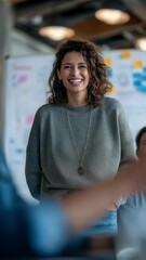 Poster - Professional businesswoman confidently smiling during collaborative project meeting, wearing casual gray sweater and jeans, standing near whiteboard with hands in pockets