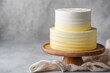© Irina - A beautifully crafted two-tier cake features a gradient of yellow and white frosting, showcased on a wooden stand, perfect for any celebration.