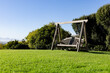 © Wavebreak Media - wooden swing bench is resting on green lawn under clear blue sky, shrub and tree border