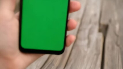 Using modern touchscreen mobile phone with green screen for advertising over textured wooden surface outside.