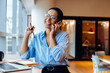 © (JLco) Julia Amaral - Smiling businesswoman talking on phone at desk with laptop and notes