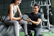 © itchaznong - Personal Trainer Assisting Female Client with Dumbbell Exercise. Focus on Strength Training.
