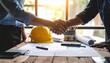 © Aura - Two individuals—one in a suit, the other in a hi-vis vest—shake hands over a table with construction helmets and documents, symbolizing partnership, project agreement, or site collaboration.