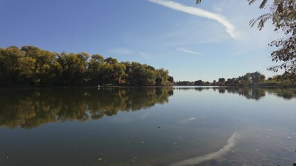 Wall Mural - Calm lake mirrors golden autumn trees beneath a clear blue sky streaked with wispy white clouds