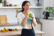 © nenetus - Kind sporty woman drinking a healthy green smoothie standing in the kitchen at home.