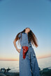 © SHOTPRIME STUDIO - lifestyle woman in modern boho-western denim street style with flowing hair stands by the ocean at sunset, captured in vivid film color tones for a natural urban vibe