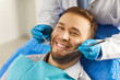 © Studio Romantic - Dental health. Man sits comfortably in dentists chair, showing off white smile that exudes confidence. Dentist holds special tools in his hands for preventive and therapeutic examination of teeth.