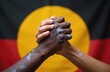 © Maryna - Close-up of two hands clasped together, one dark-skinned with white paint, against the Australian Aboriginal flag. Symbolizes reconciliation, unity, and understanding between cultures.