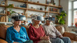 © Domingo - Three joyful senior people, two women and one man, are comfortably seated on a living room couch, each wearing a virtual reality headset, immersed in a shared digital experience