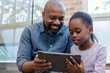 © Wavebreak Media - African American father and daughter sitting on couch by window at home sharing tablet content