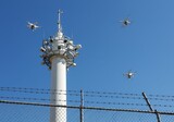 Drones flying around a communication tower with a barbed wire fence