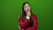 © Krakenimages.com - Young woman in red jacket pondering against green background, exuding elegance and confidence, while maintaining a thoughtful expression with hand on chin.