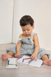 © Tuan - a baby sitting on the floor, writing in a notebook with a pen. The background of the image is a wall.