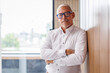 © David - Portrait of Happy mature older male entrepreneur standing with crossed arms smiling confident at camera. Latin or eastern middle age male ceo leader business man standing in office. Copy space