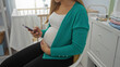 © Krakenimages.com - Pregnant woman sitting in a bedroom gently holding her belly with one hand and using a smartphone with the other in a cozy home interior next to a baby cradle.