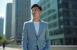 © miss irine - Young Chinese man in light blue suit and white undershirt stands confidently on city street. Handsome executive looks away from camera with modern skyscrapers background in sunny day.
