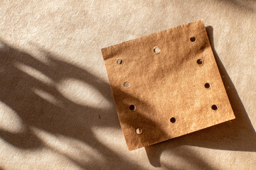 Aufkleber - Square brown paper with perforated edge and soft shadow, casting gentle lines on textured surface, minimal and natural style, warm sunlight, creative background