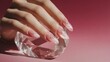 © อภิรักษ์ อุ๋ยสกุล - A woman's manicured hand rests gracefully upon a faceted crystal, showcasing elegant and transparent nail art against a soft pink backdrop in a studio setting.