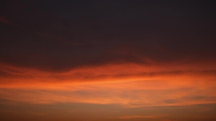 Wall Mural - a dramatic sunset sky timelapse with deep orange and burnt sienna clouds stretching across a darkeni