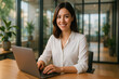 © Design studio - Happy young woman in white shirt working on laptop in bright indoor office with calm background