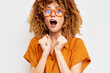 © SHOTPRIME STUDIO - Excited woman with curly hair and glasses expressing joy against a plain background Bright orange attire enhances her vibrant personality and enthusiasm, capturing a sense of wonder