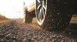 © Mid - Close up of a car wheel on a gravel road with dirt and small rocks spraying into the air. Sunlight illuminates the scene, emphasizing the motion and texture.