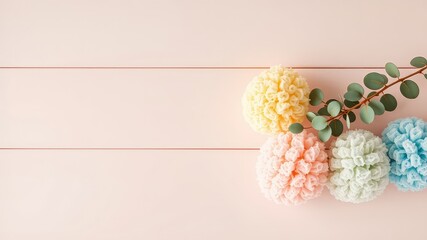 Poster - Soft and Subtle Pastel Colored Pompoms with Fresh Greenery Resting on a Light Wooden Surface, Ideal for Gentle and Delicate Designs