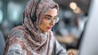 © Johannes - Muslim business woman with headset working in office. Happy arab woman working in company service center wearing headphone and using computer helping solving client problem. Islamic woman., no logos,