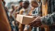 © Johannes - charity, donation and volunteering concept - close up of male volunteer's hands holding box with food over group of people at distribution or refugee assistance center, no logos, no brands