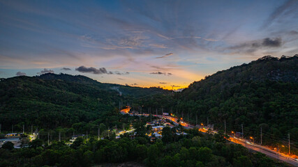 Wall Mural - Aerial hyper lapse view of A breathtaking sunset paints the sky in vivid hues of orange and blue over a coastal town, with lush green hills framing the scene. cloud in dramatic sunset over the ocean